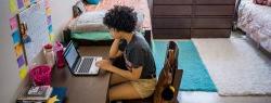 African-American female in dorm room at desk working on laptop